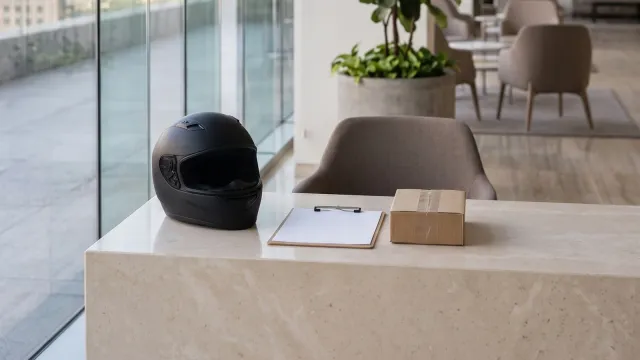 Casco de motociclista, planilla y paquete sobre el mostrador de recepción de una oficina